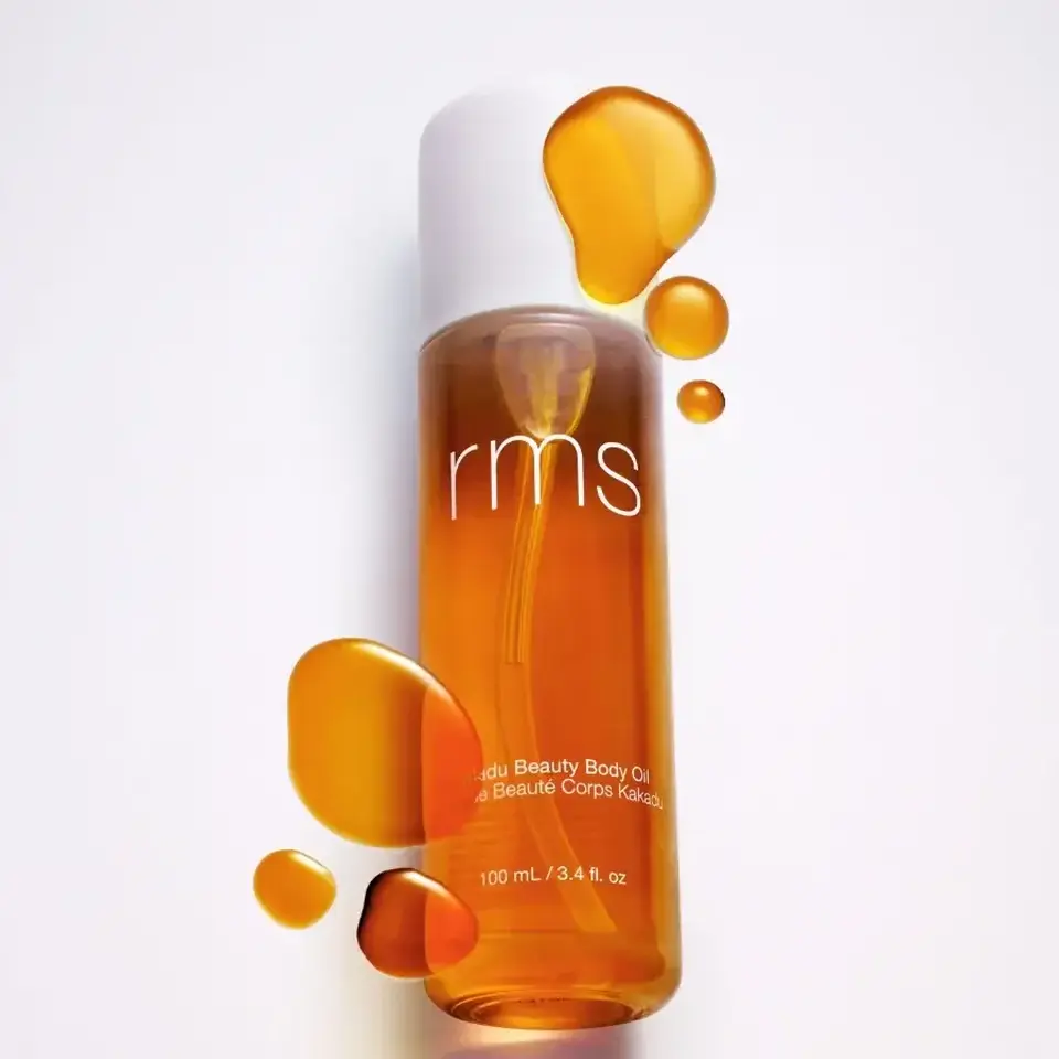 RMS Kakadu Beauty Body Oil, 100 mL bottle with oil droplets on white background.