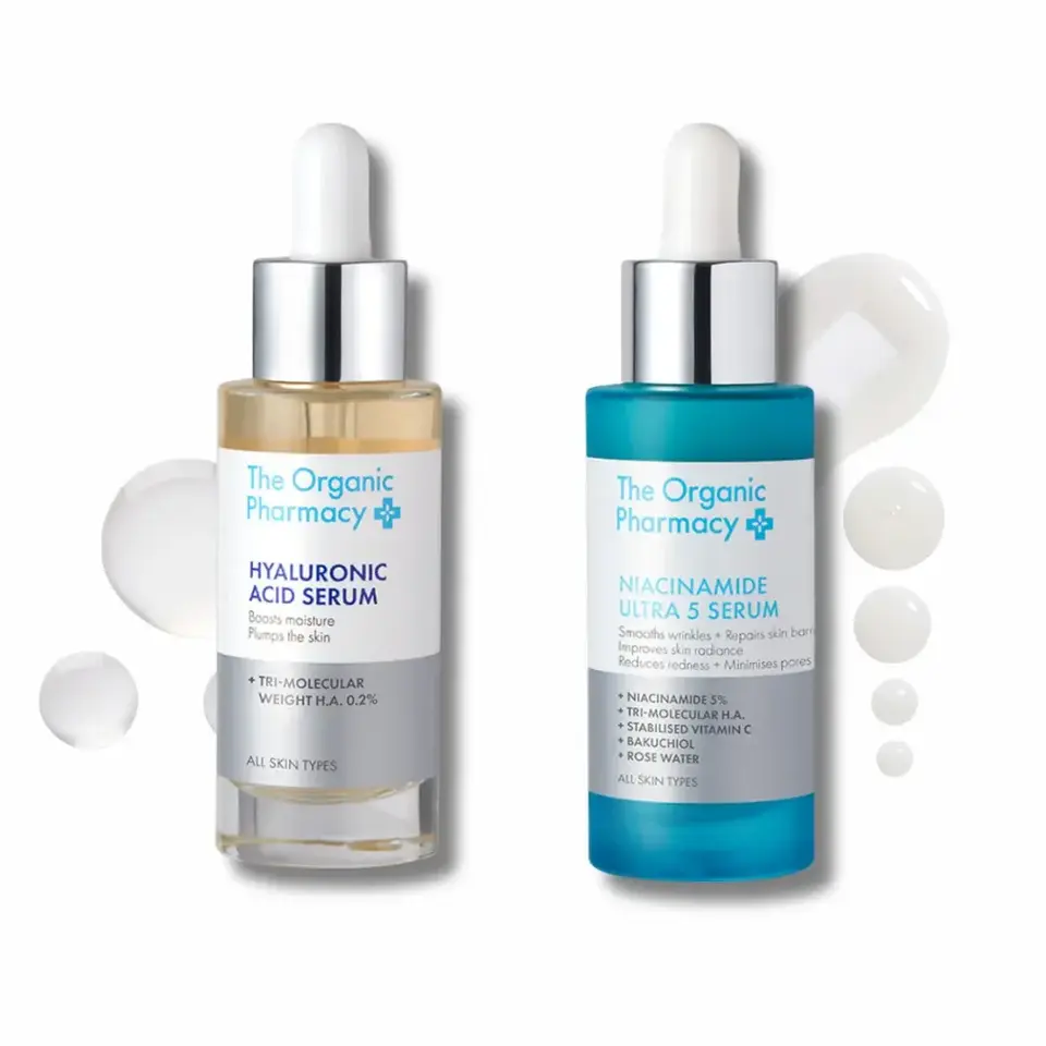 Two bottles of The Organic Pharmacy serums with droppers and liquid droplets.