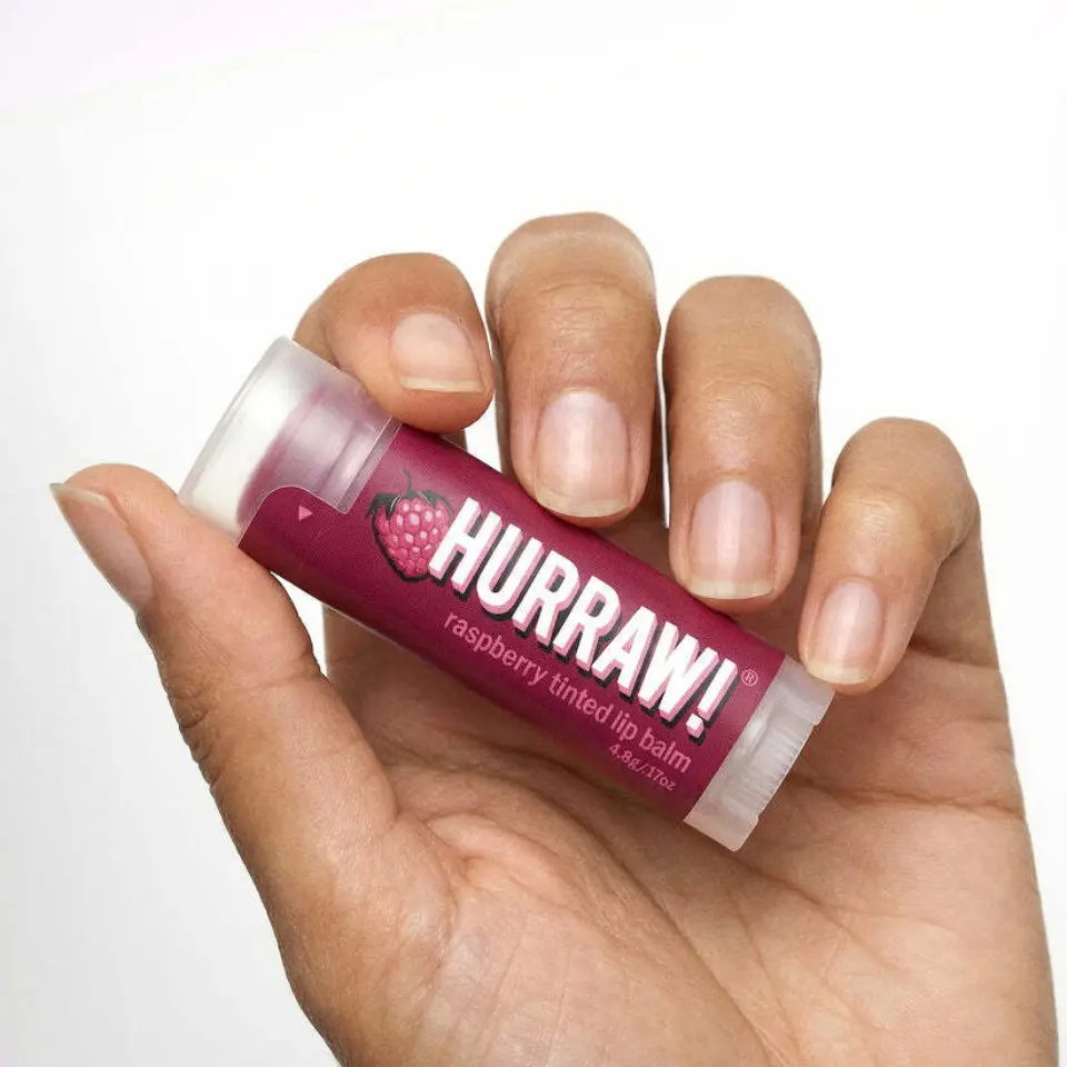 Hand holding Hurraw! raspberry tinted lip balm.