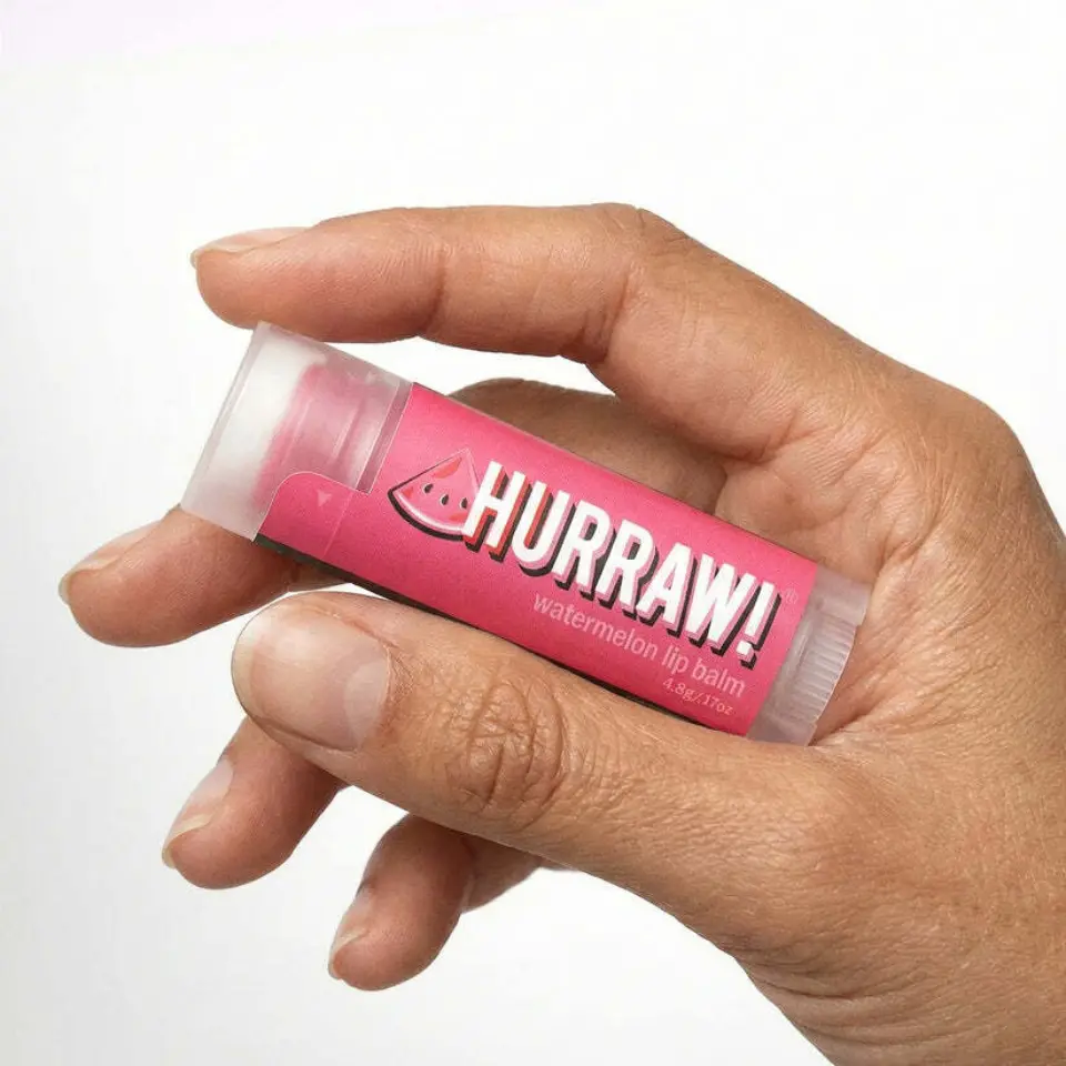 Hand holding Hurraw! watermelon lip balm tube.