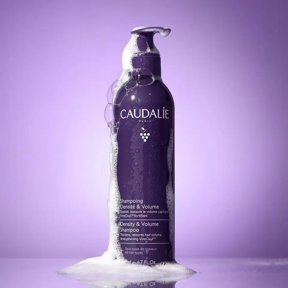 Caudalie Density & Volume Shampoo bottle with foam, purple background.