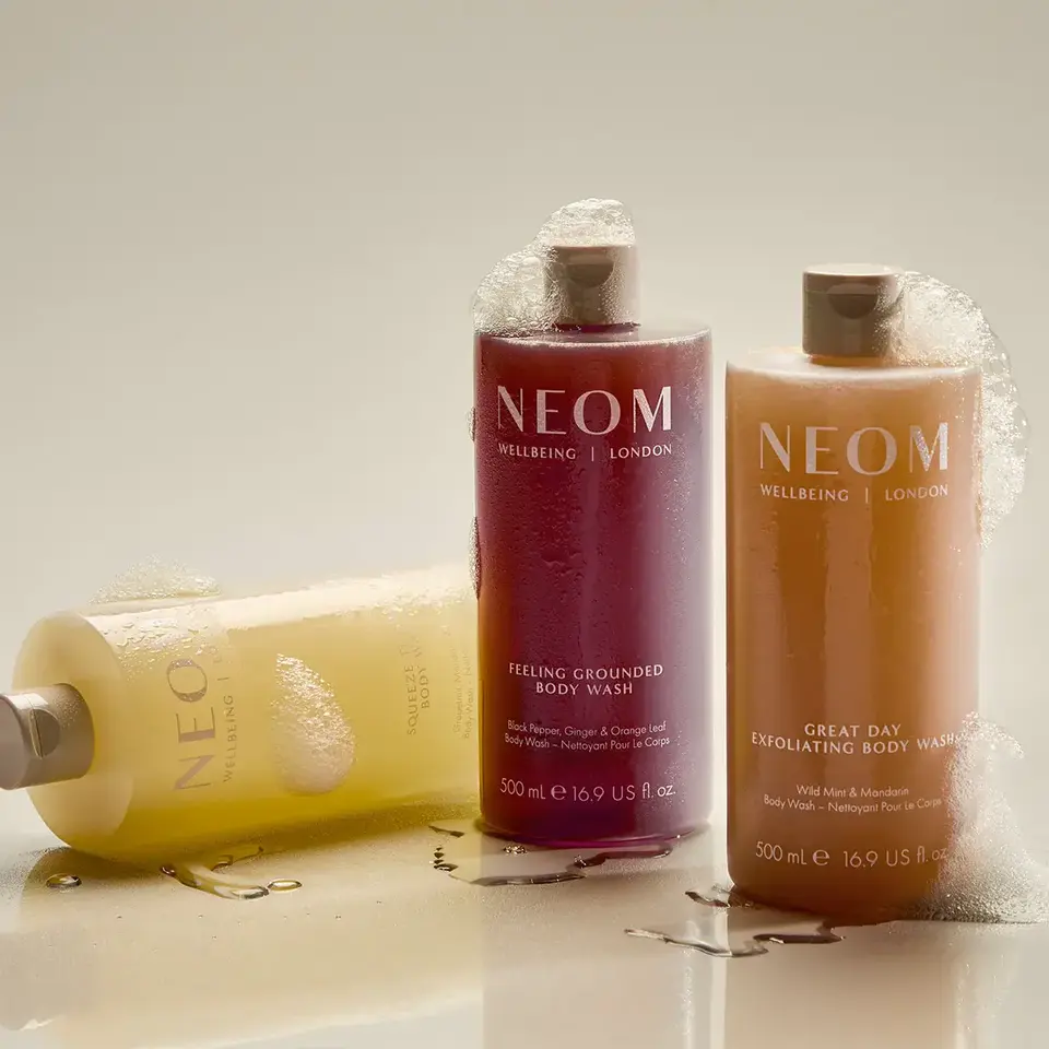 Three NEOM body wash bottles with foam, labelled "Feeling Grounded" and "Great Day".