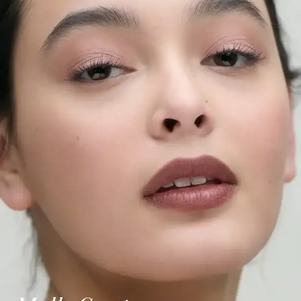 Close-up of a person with natural makeup. Text: "Mallo Coast".