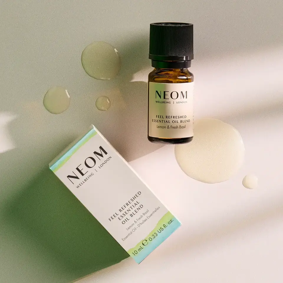 NEOM Feel Refreshed essential oil blend bottle and box on a light surface with oil droplets.
