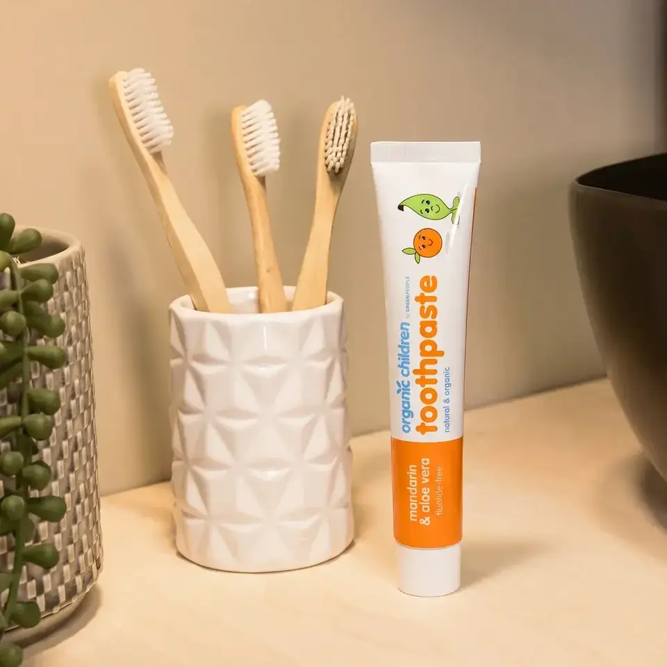 Tube of organic children's toothpaste beside bamboo toothbrushes in a holder.