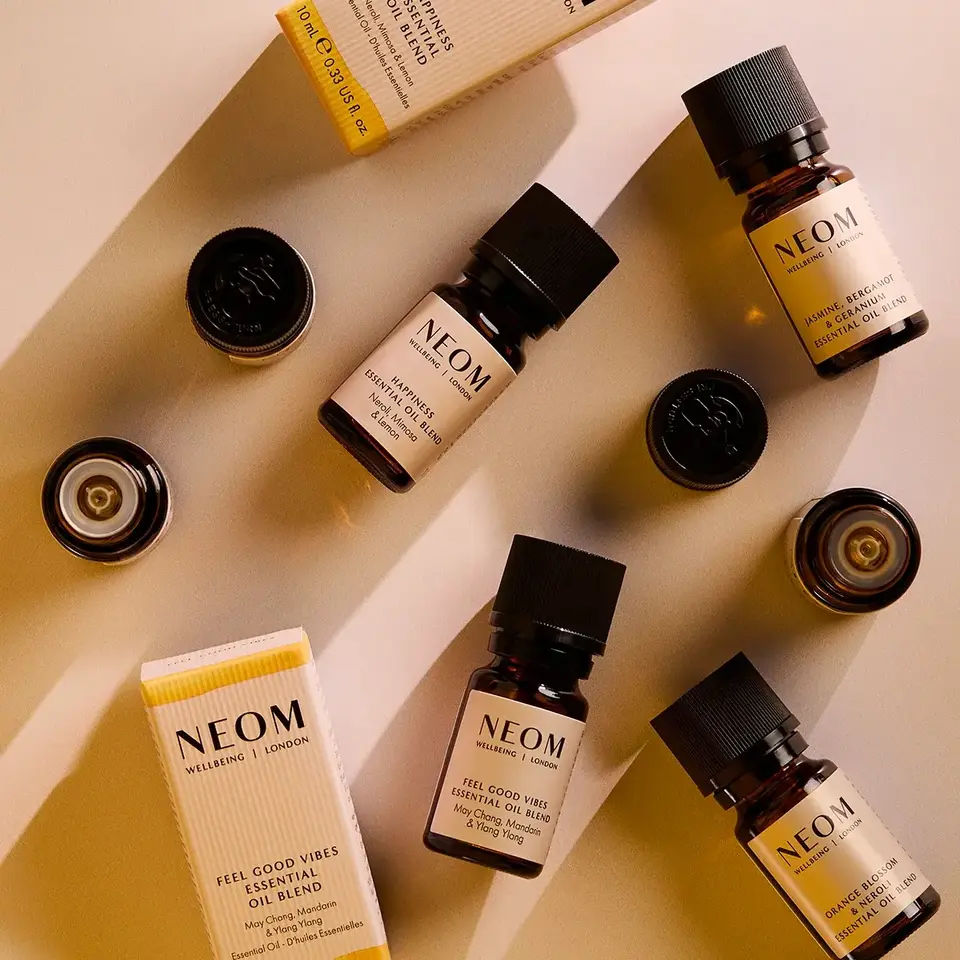 Neom essential oil bottles and packaging on a beige surface.
