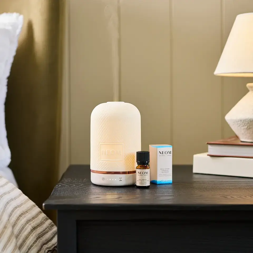 Diffuser and essential oil on bedside table with lamp and books.