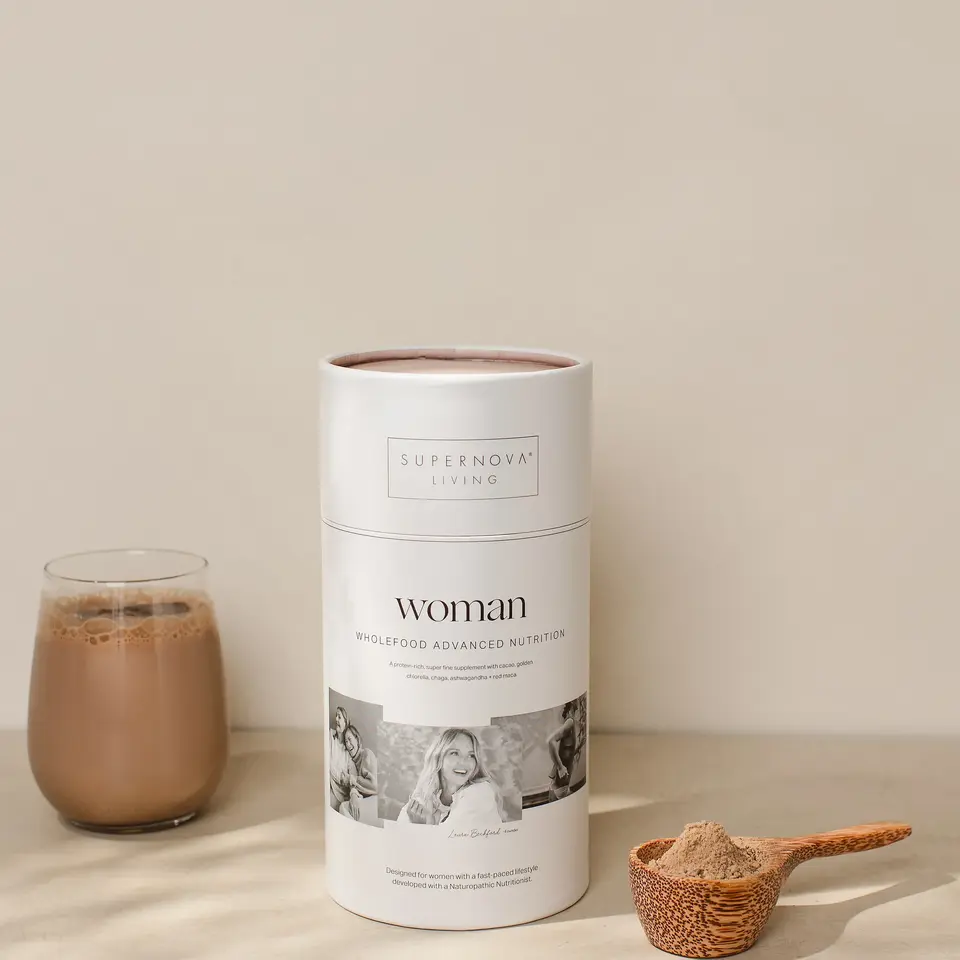 Supernova Living Woman supplement with a glass of chocolate drink and a wooden scoop of powder.