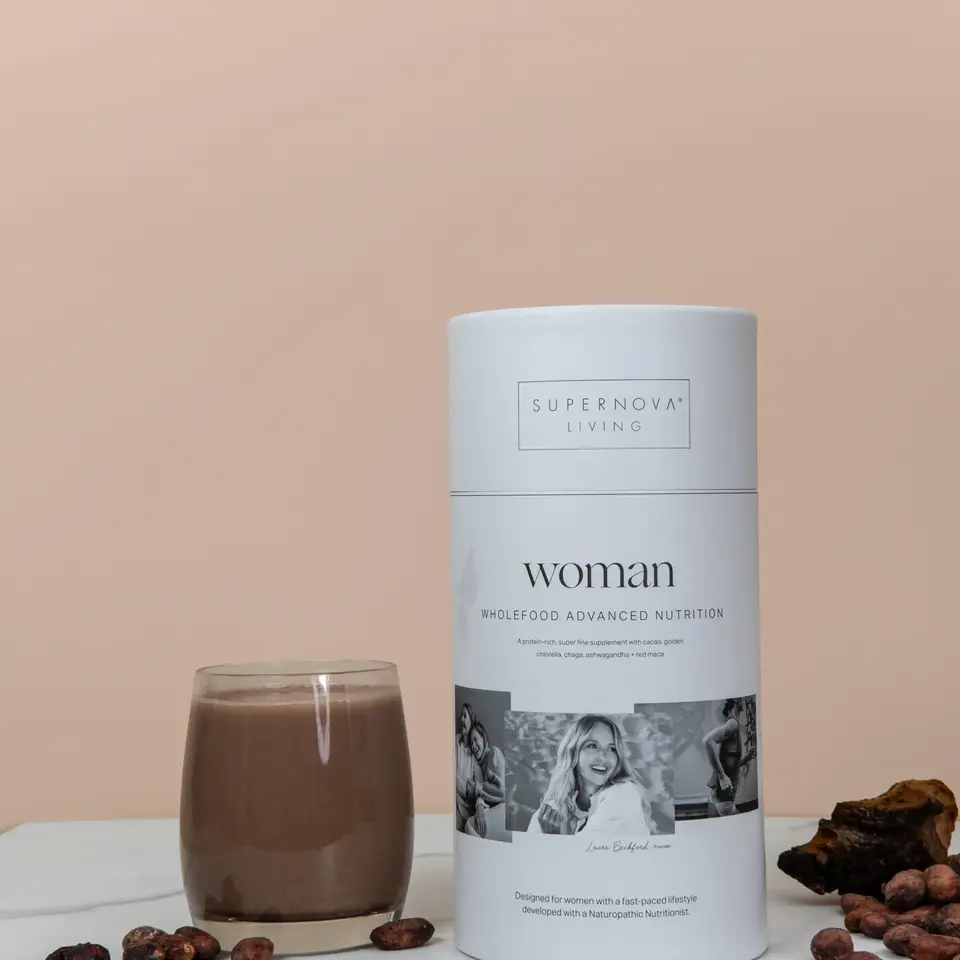Supernova Living Woman nutrition powder with a glass of chocolate drink on a marble surface.