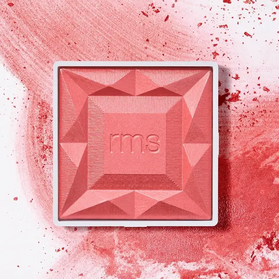 Square pink blush with "rms" embossed, surrounded by scattered powder.