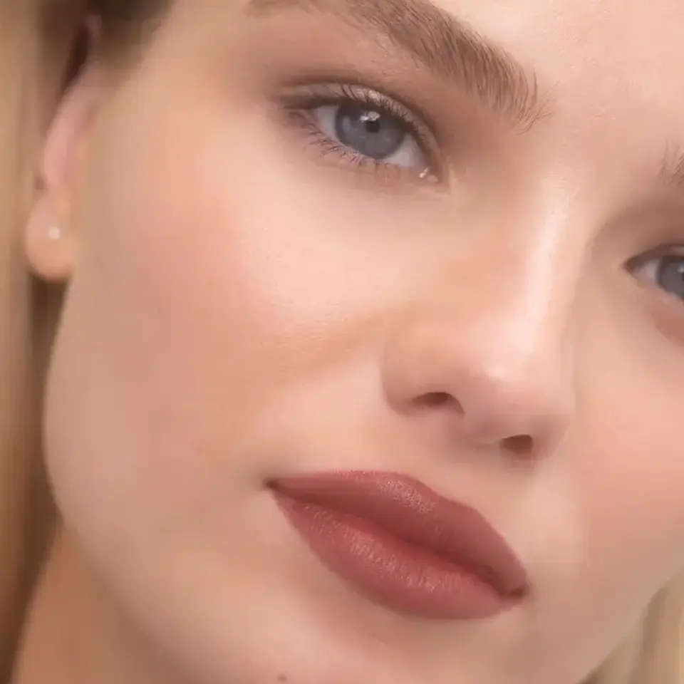 Close-up of a person with smooth skin, red lipstick, and text "NAOMI" in the corner.