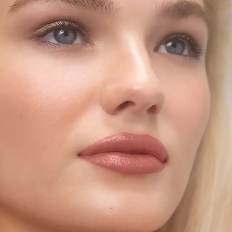 Close-up of a person with smooth skin and natural makeup. Text: MAE.
