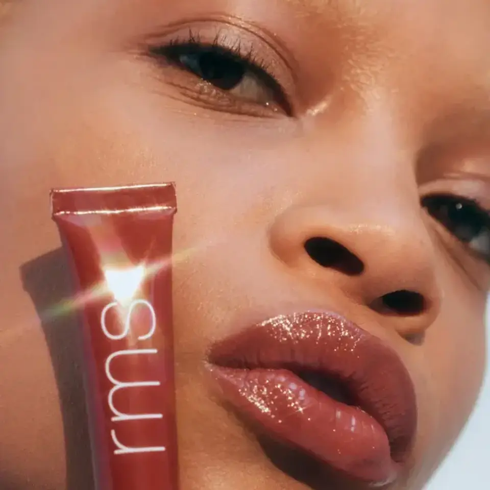 Person with glossy lips holding RMS Liplights tube. Text: "RHAPSODY".