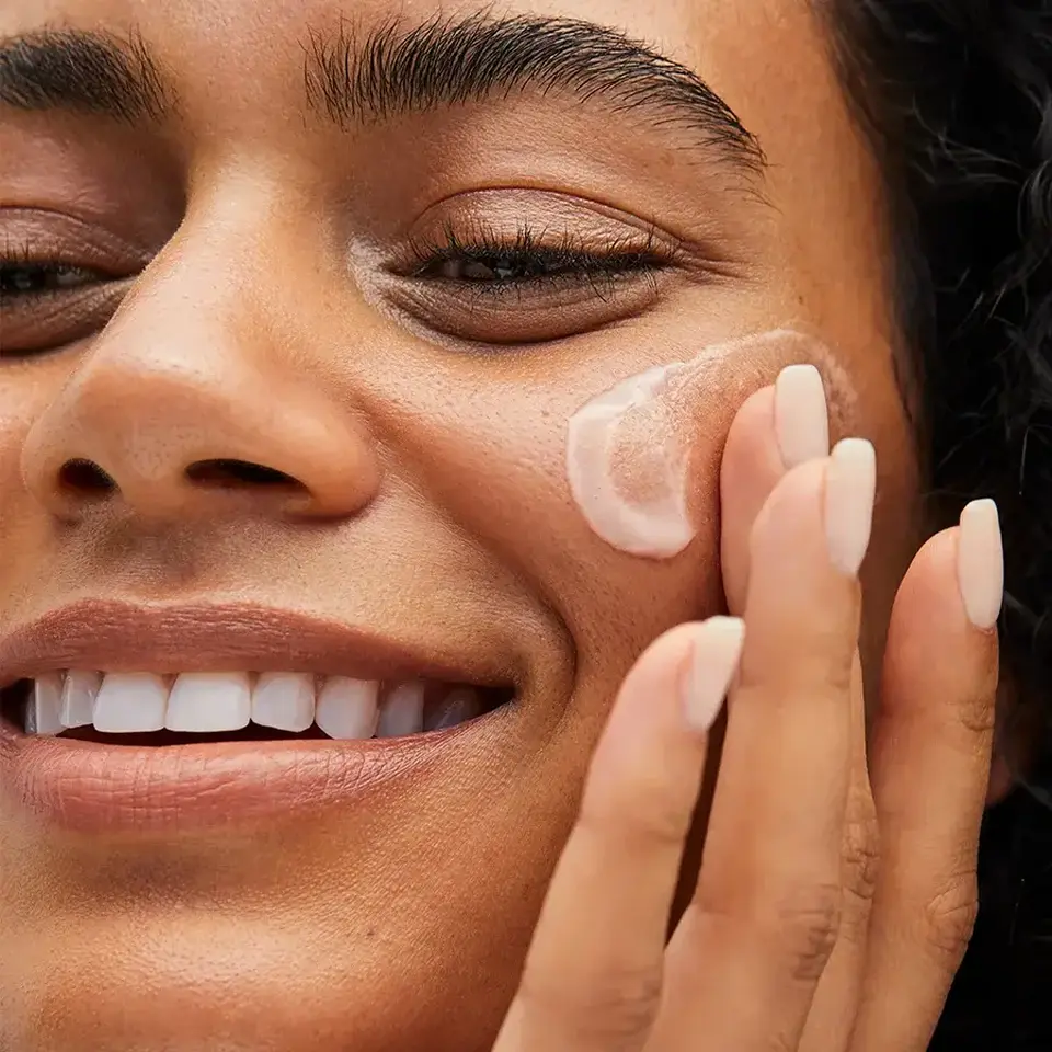 Person applying cream to cheek with fingers.