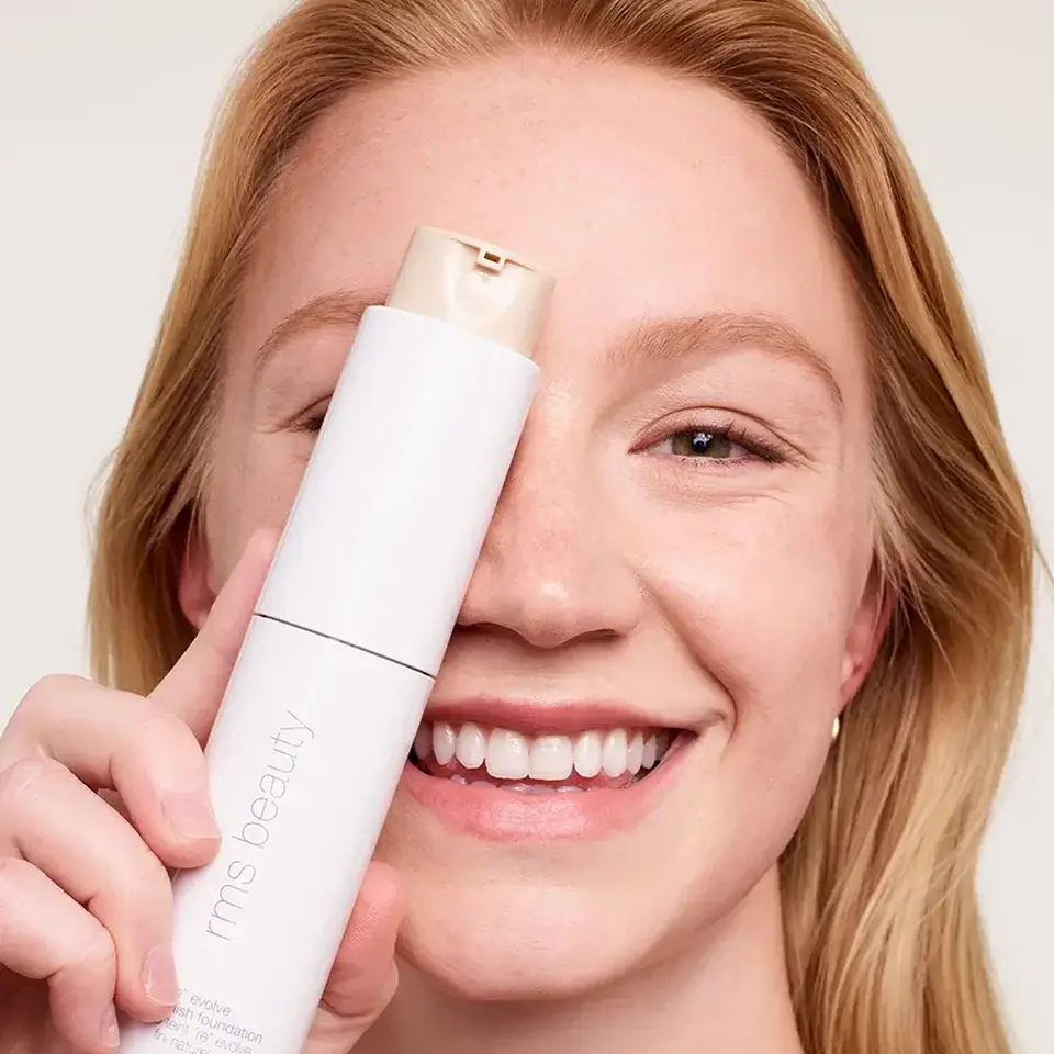 Smiling person holding rms beauty foundation bottle.