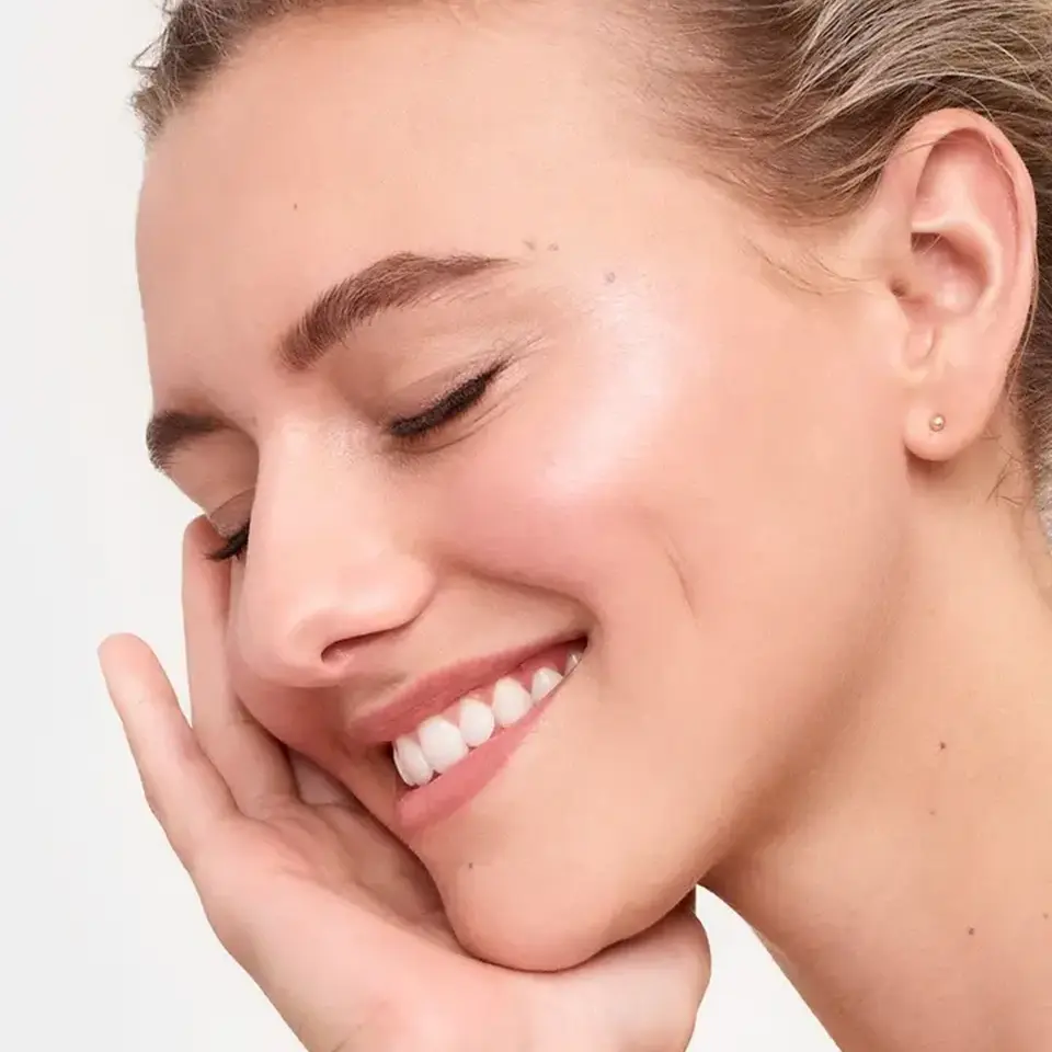 Woman with closed eyes smiling, touching her cheek.