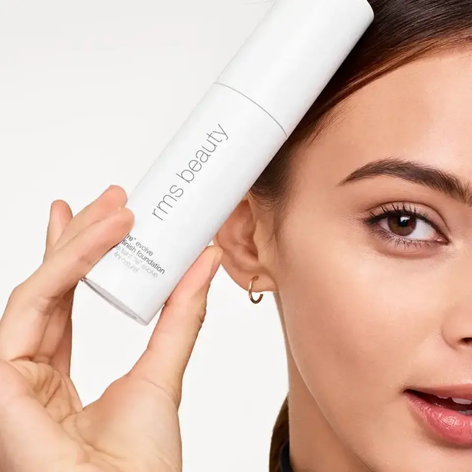 Woman holding rms beauty foundation bottle near face.