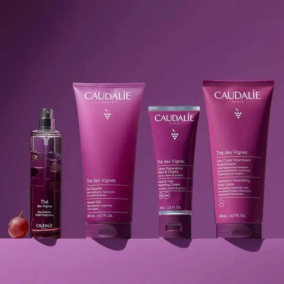 Caudalie Thé des Vignes products: fragrance, shower gel, hand cream, body lotion on purple background.