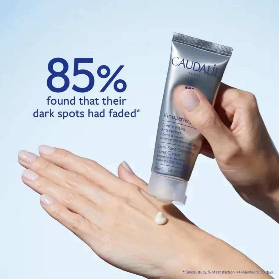 Hand applying Caudalie Vinoperfect cream. Text: "85% found dark spots faded".