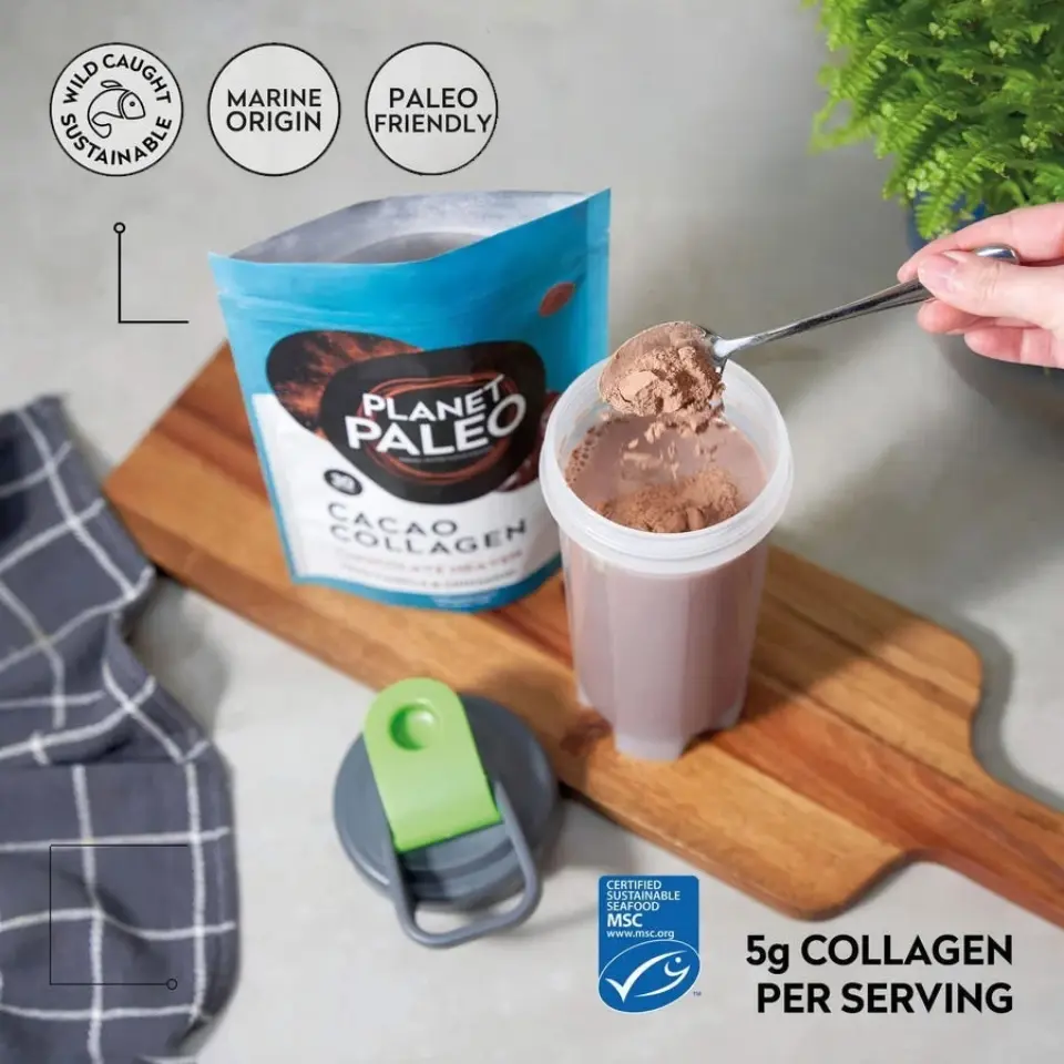 Planet Paleo Cacao Collagen powder being added to a shaker on a wooden board.