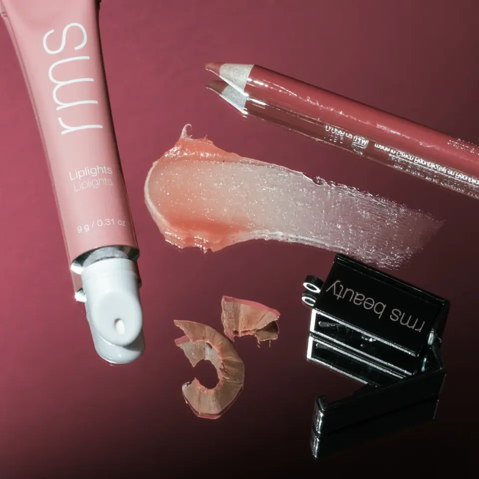 Lip balm tube, lip pencil, sharpener, and balm smear on a reflective surface.
