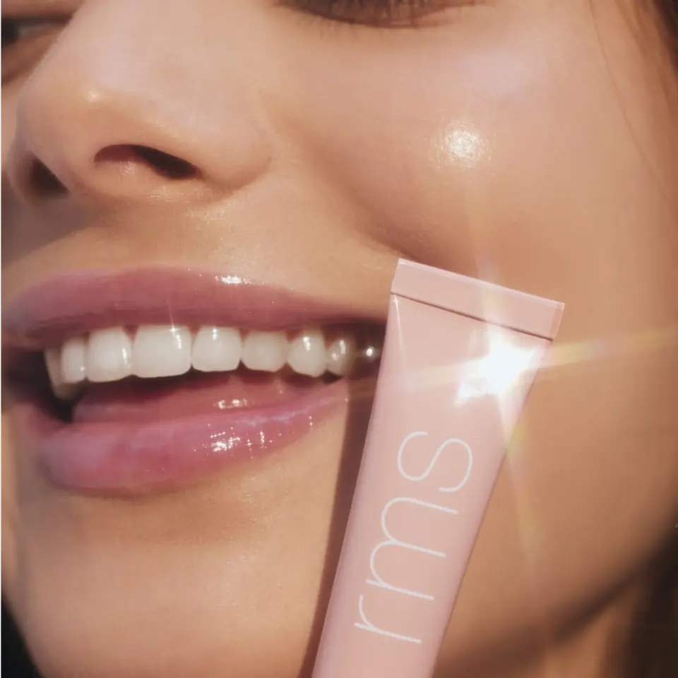 Close-up of a smiling person holding a pink tube labelled "rms" near their face.