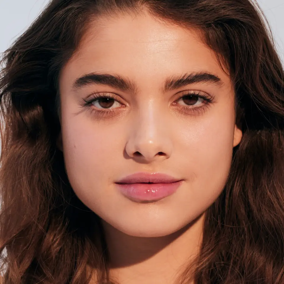 Woman with long brown hair and clear skin, wearing light pink lip gloss.