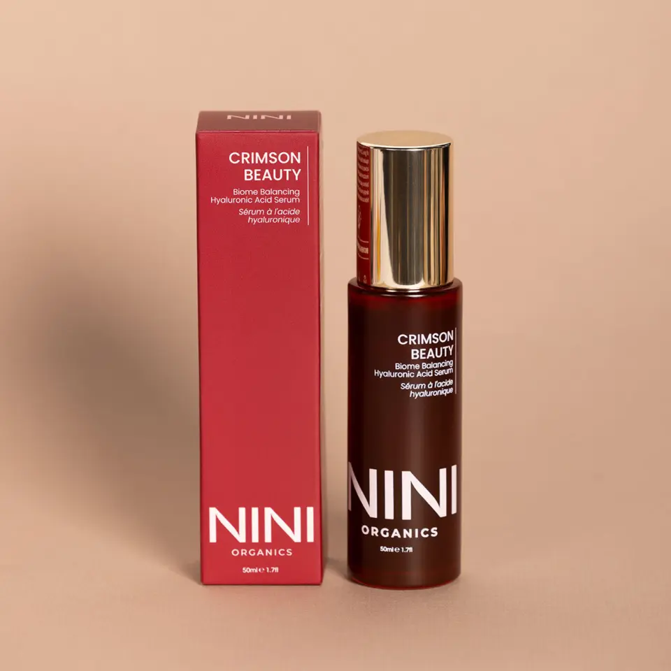 Crimson Beauty serum bottle and box on beige background. NINI Organics branding visible.