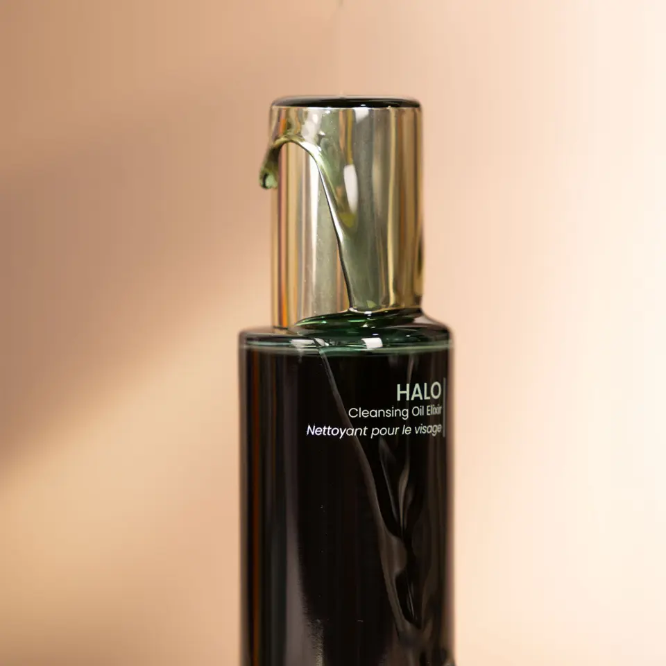 Halo Cleansing Oil Elixir bottle with gold pump on beige background.