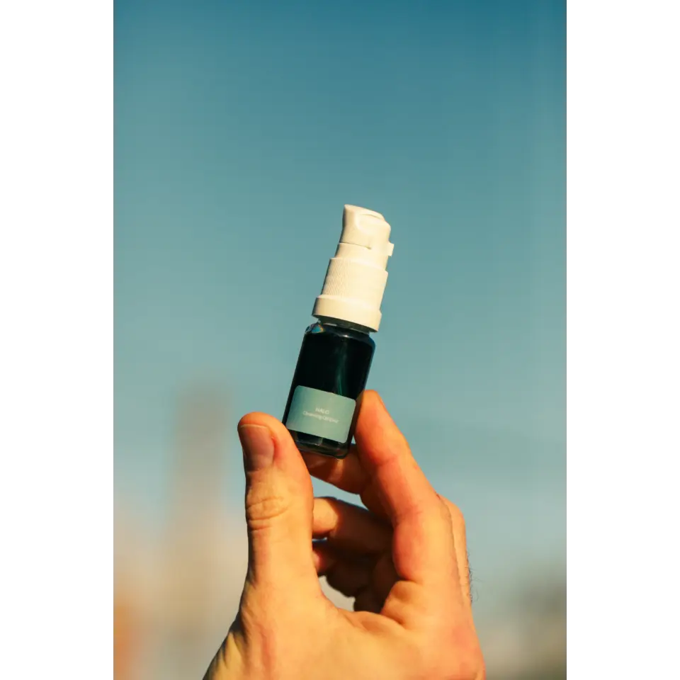 Hand holding a small blue-labelled spray bottle against a clear sky.