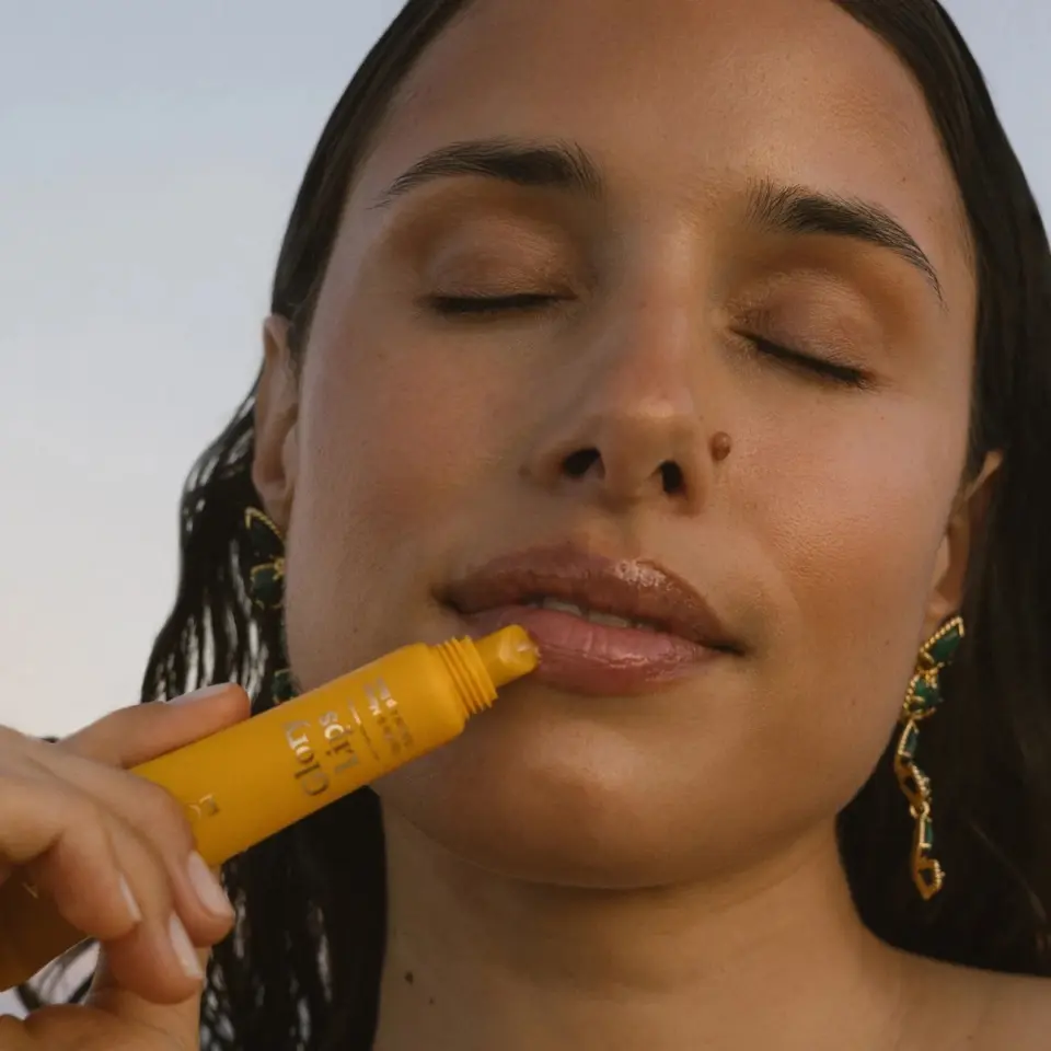 Woman applying yellow lip balm with eyes closed.