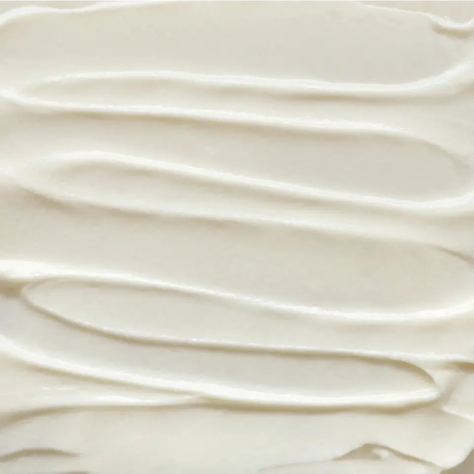 Creamy white skincare product texture with smooth, wavy lines.