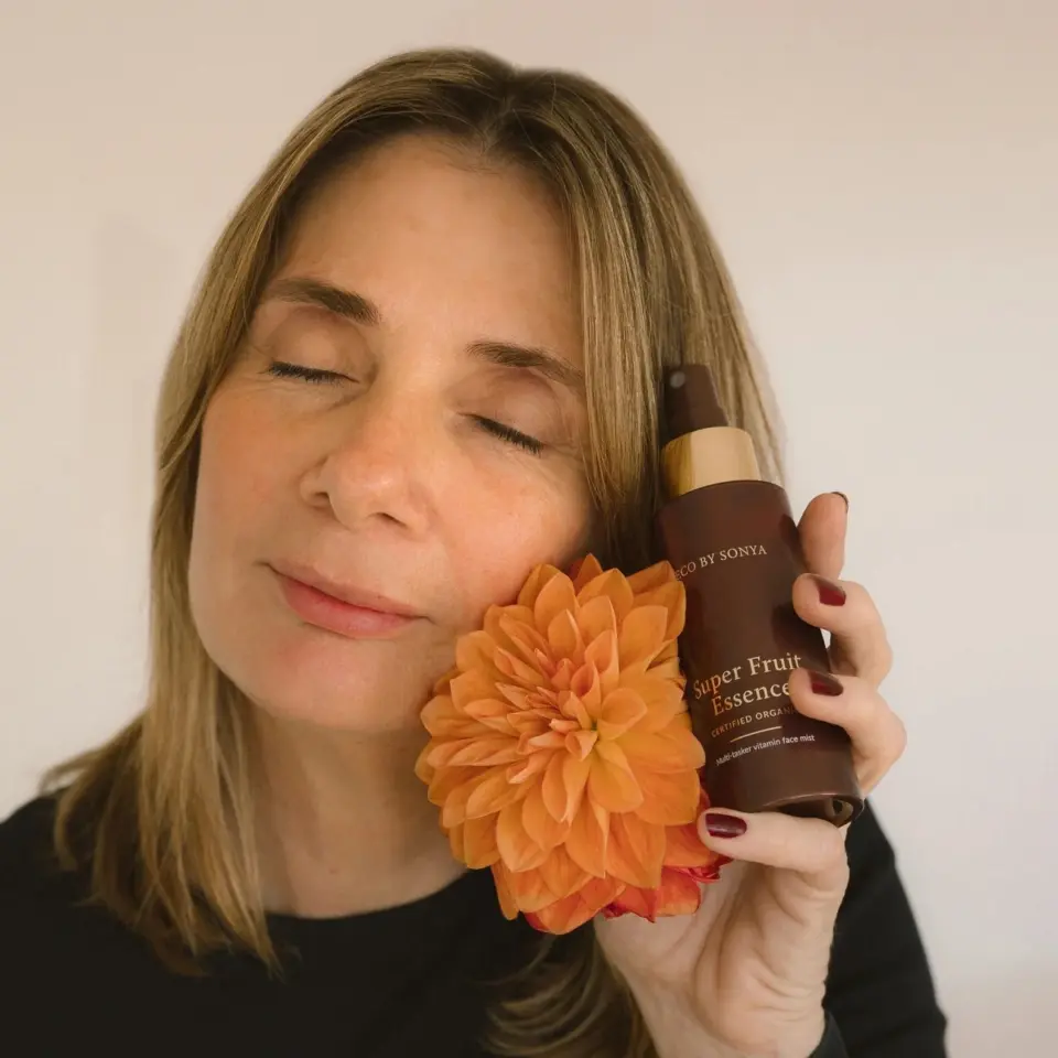 Woman holding Eco by Sonya Super Fruit Hydrator bottle and orange flower.