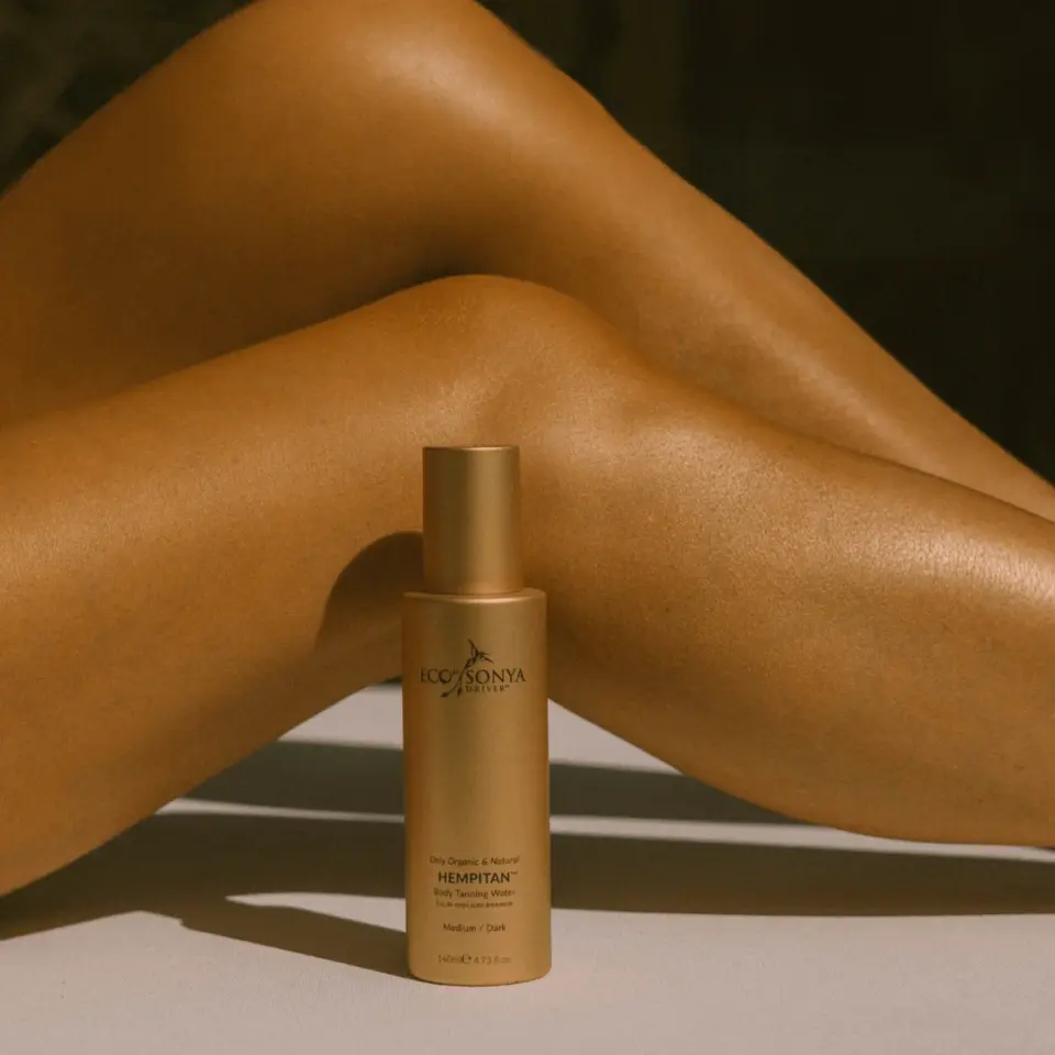 Tanned legs crossed, Eco by Sonya Hempitan bottle in foreground.