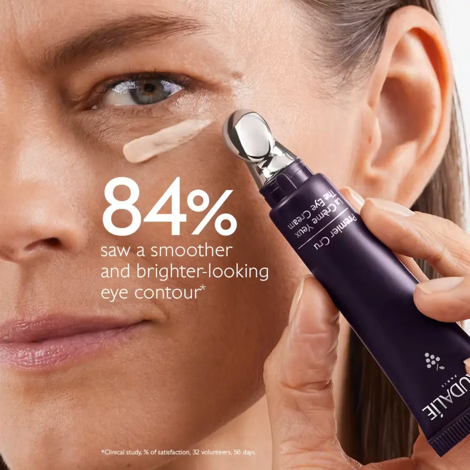 Woman applying eye cream with metal applicator, text: "84% saw smoother, brighter eye contour".