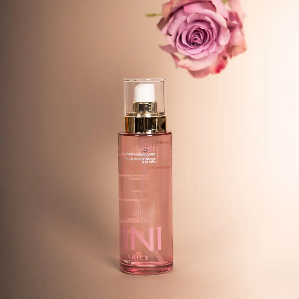 Pink bottle of rose petal hydrating mist with a purple rose above.