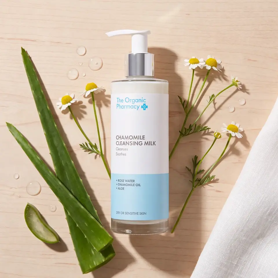 Chamomile Cleansing Milk bottle with aloe and chamomile flowers on a wooden surface.