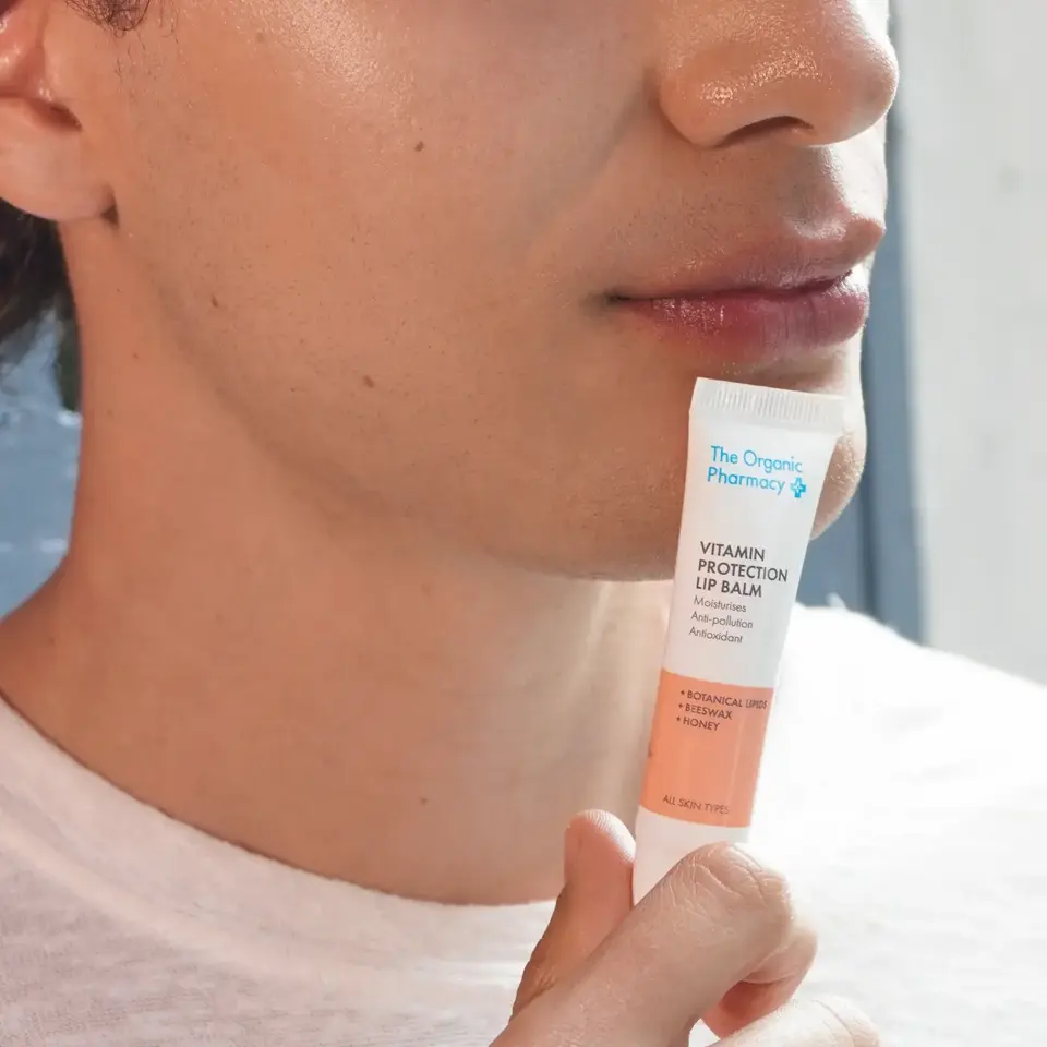 Person holding The Organic Pharmacy Vitamin Protection Lip Balm near lips.