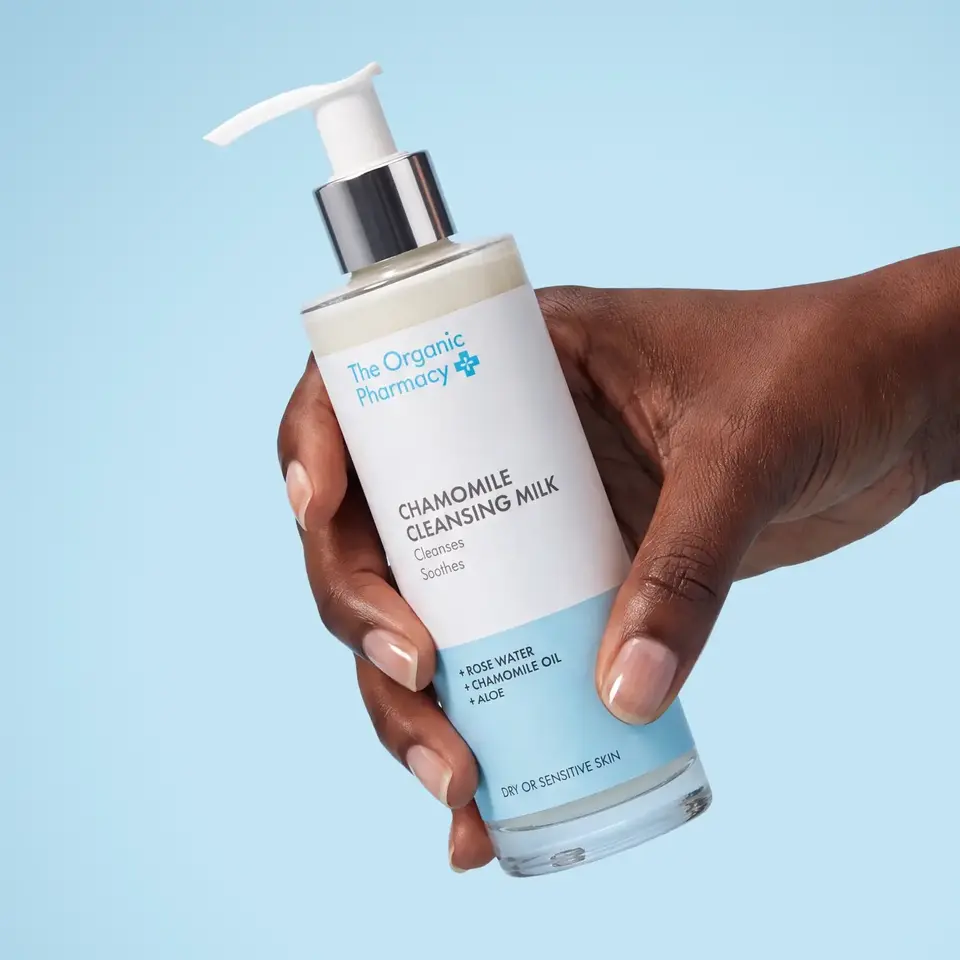 Hand holding The Organic Pharmacy Chamomile Cleansing Milk bottle.