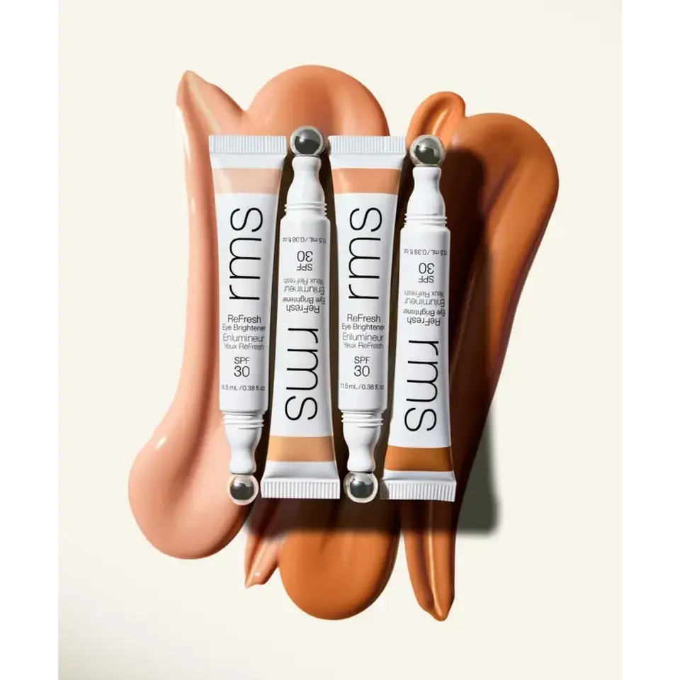 Four RMS ReFresh Eye Brightener tubes on swirled beige and brown cream background.