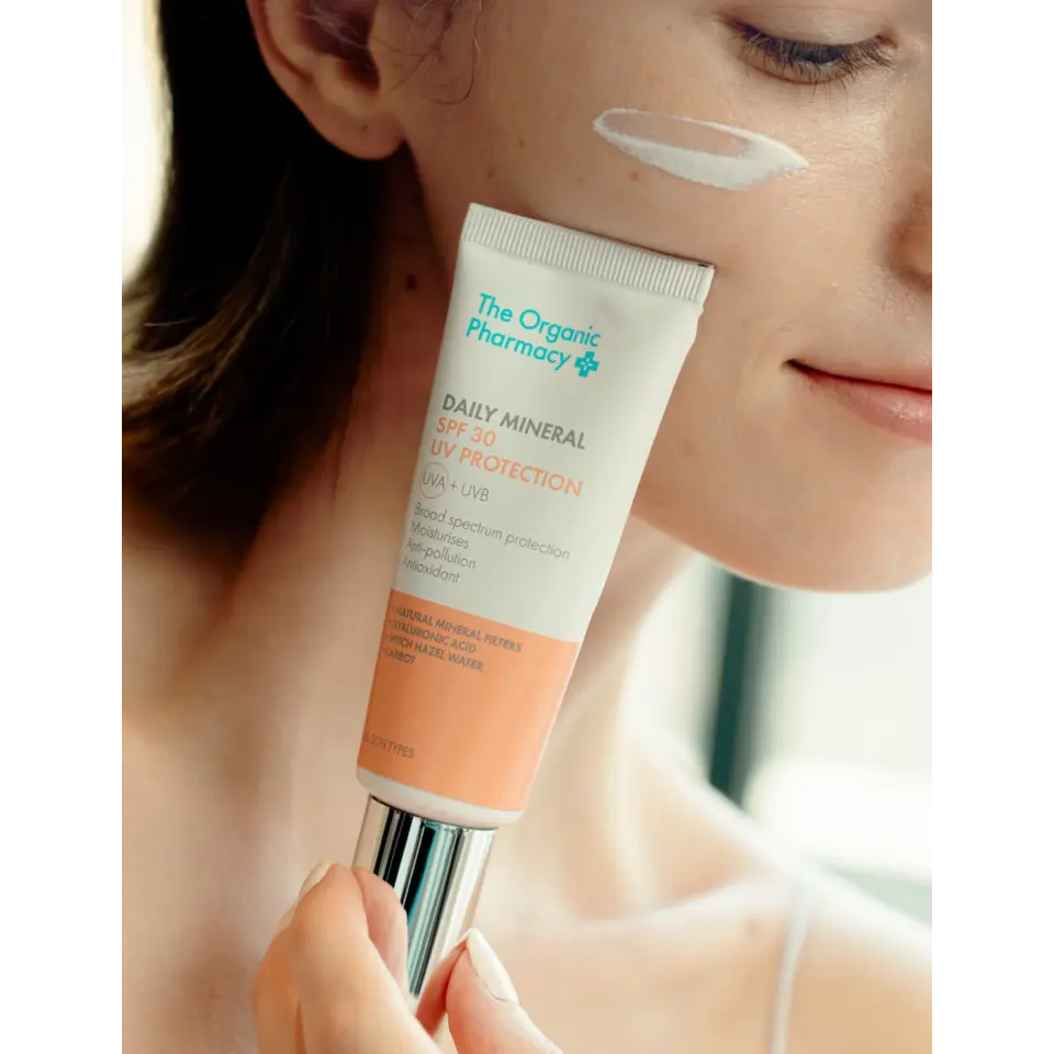 Woman applying The Organic Pharmacy SPF 30 cream to her cheek.