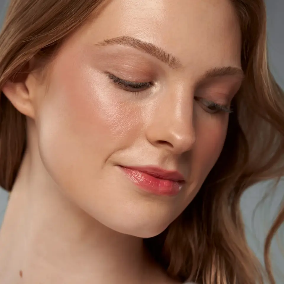 Woman with smooth, glowing skin and light makeup, looking downwards.