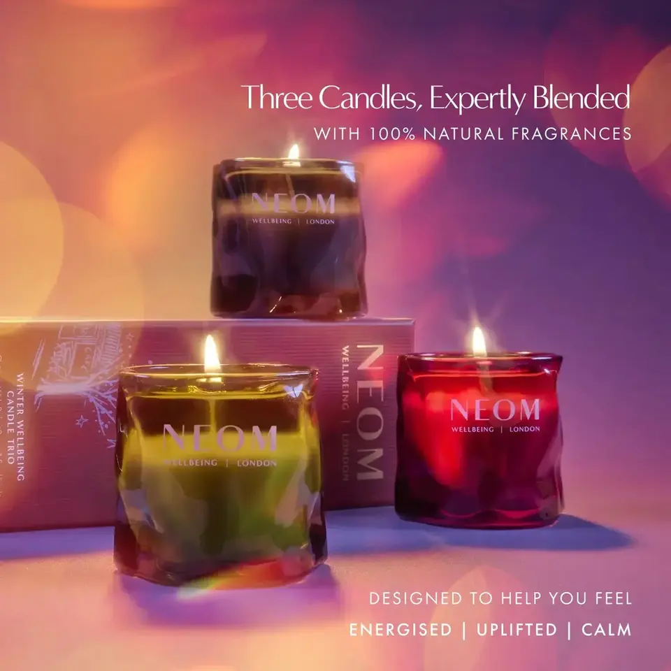 Three lit NEOM candles with packaging, text: "Energised | Uplifted | Calm".