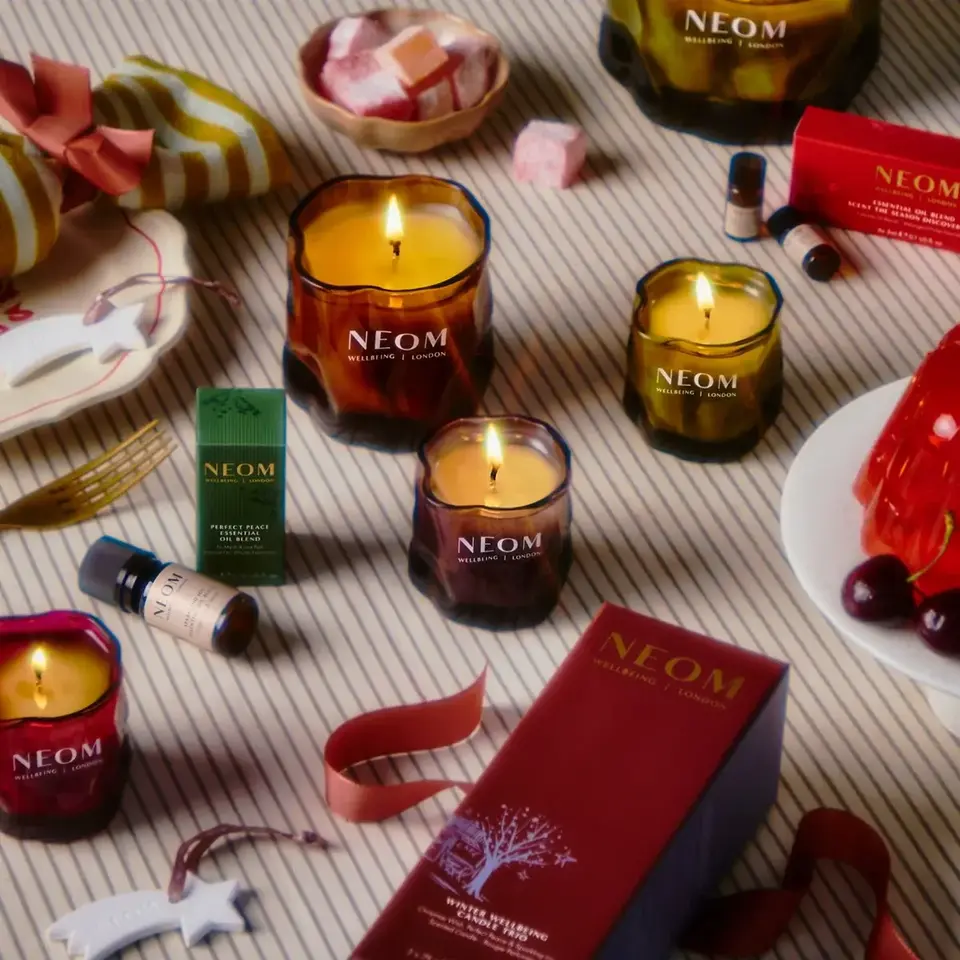 NEOM candles and products on a striped surface with decorative items and sweets.