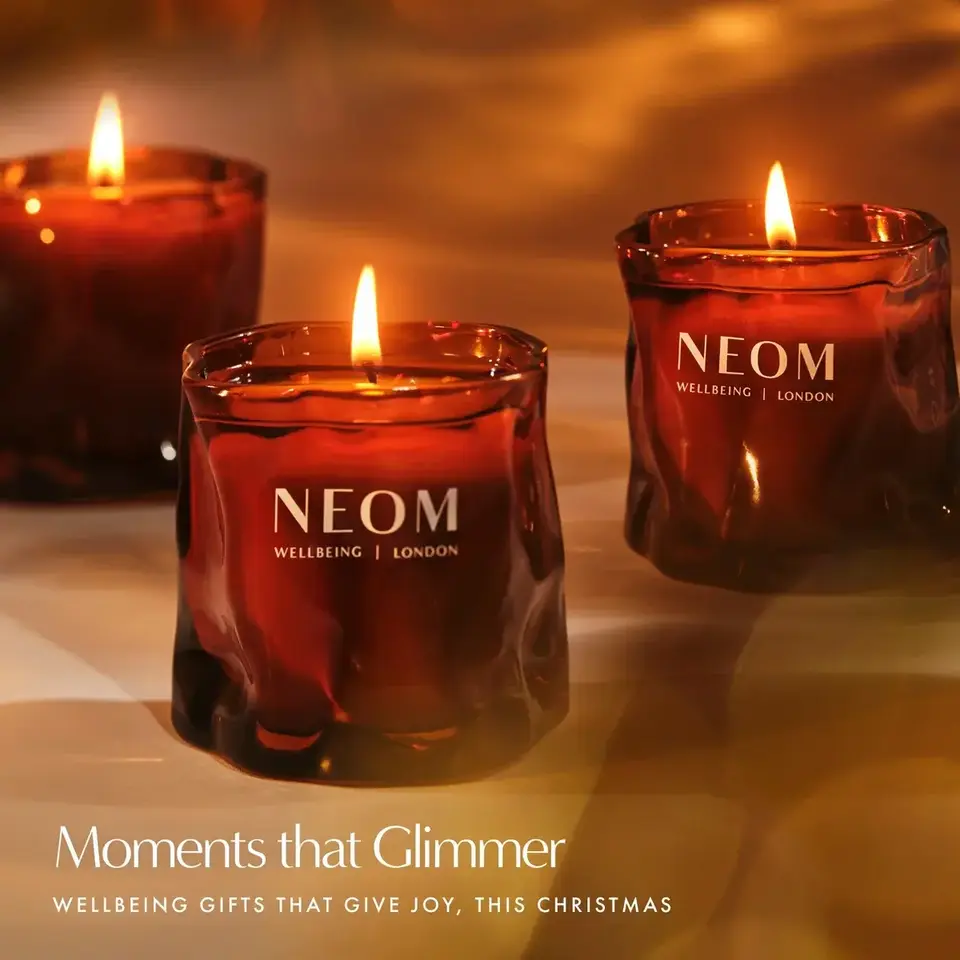 Three lit NEOM candles in amber glass jars with text: "Moments that Glimmer".