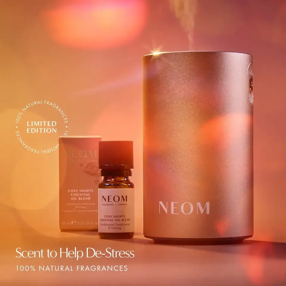 NEOM diffuser and Cosy Nights essential oil blend with packaging. Text: "Scent to Help De-Stress".