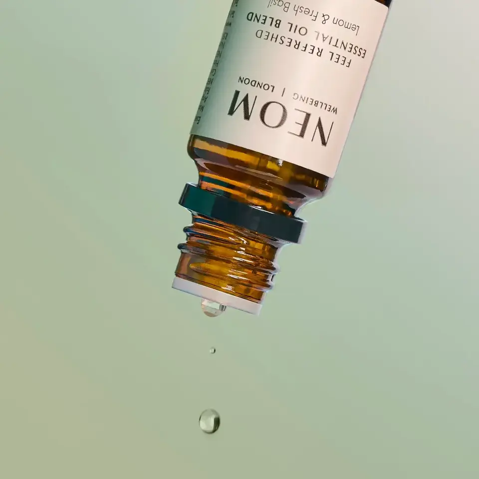 Amber bottle of NEOM essential oil with droplets falling.