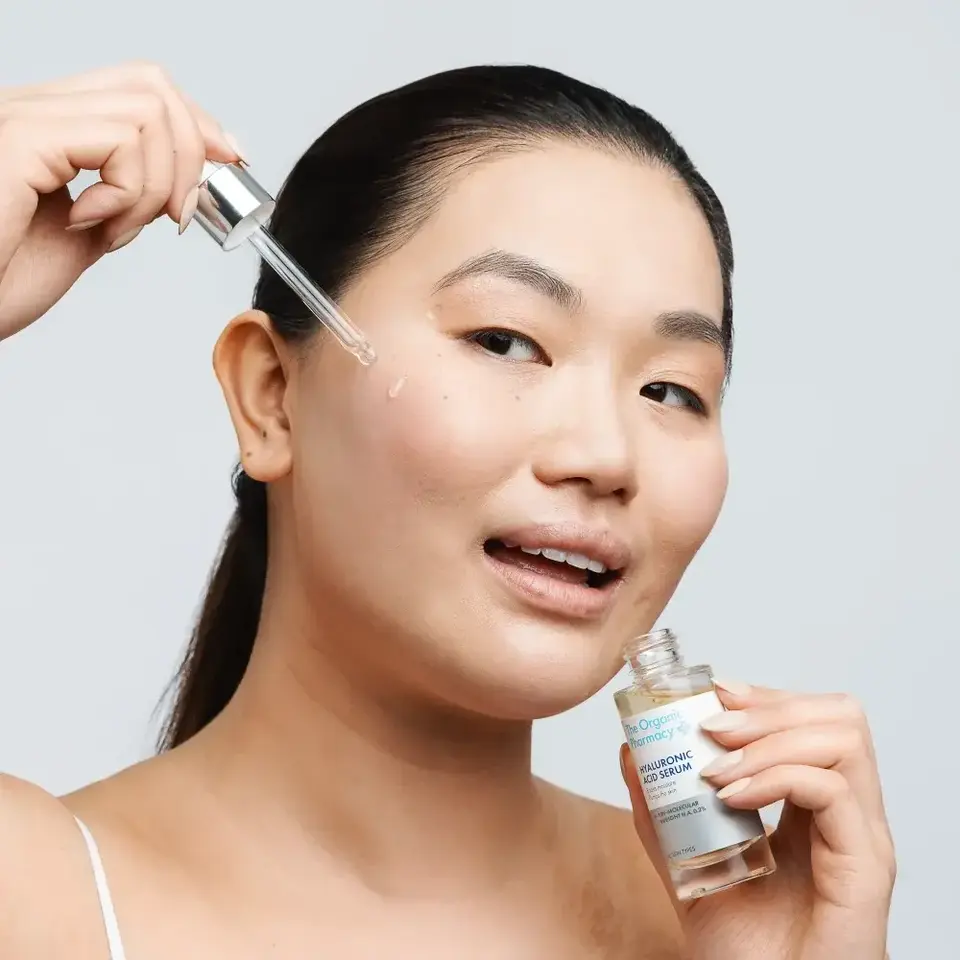 Person applying hyaluronic acid serum to cheek with dropper.