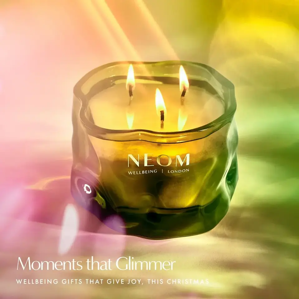 Green glass candle with three flames, NEOM branding. Text: "Moments that Glimmer".