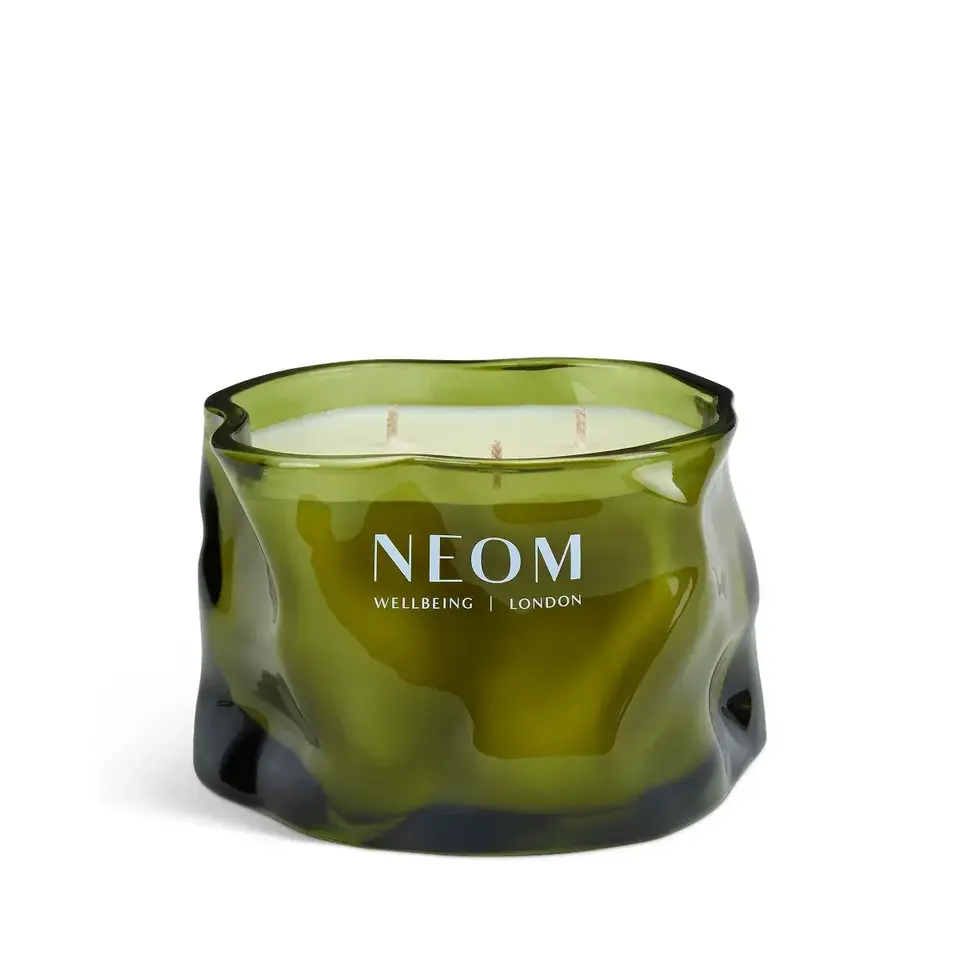 Green glass candle with "NEOM Wellbeing London" text, three wicks visible.